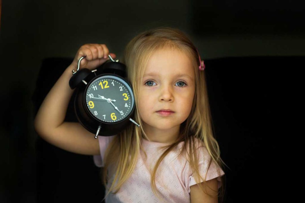 daycare aged girl holding a clock to remind her mom to be on time to pick her up