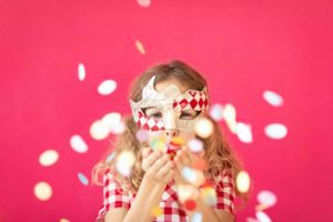 child in mardi gras costume blowing confetti