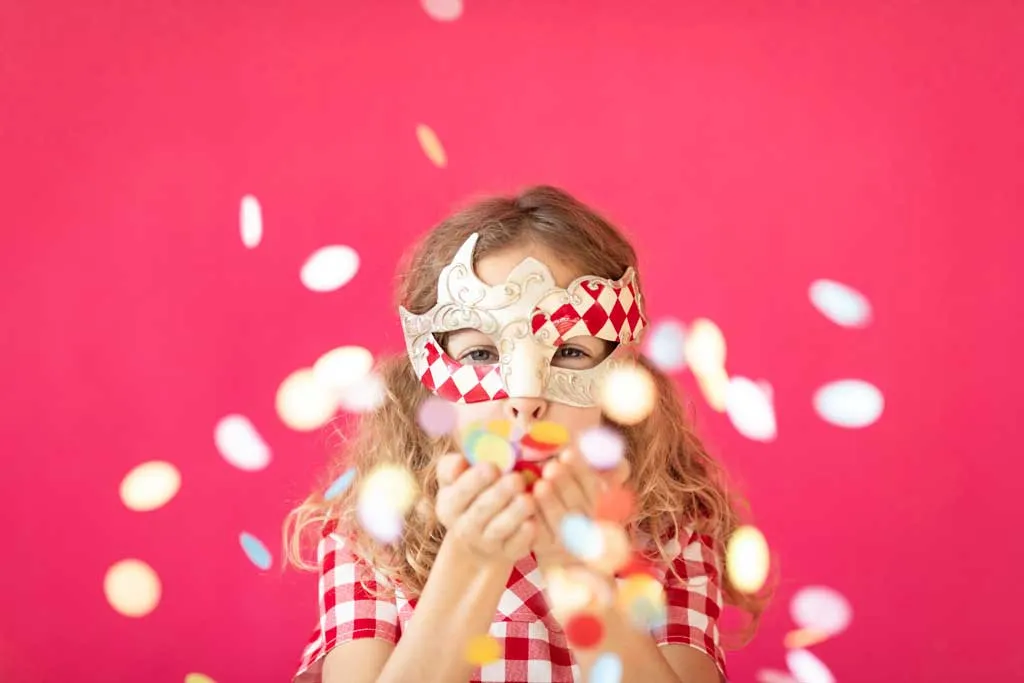 child in mardi gras costume blowing confetti