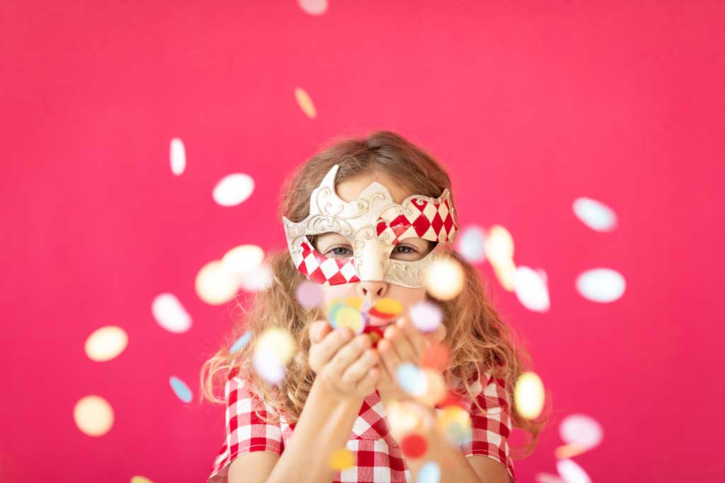 child in mardi gras costume blowing confetti